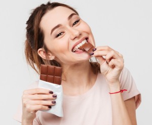 stock-photo-portrait-of-a-satisfied-pretty-girl-biting-chocolate-bar-and-looking-at-camera-isolated-over-white-766093279